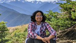 Headshot of Neha in front of mountains and trees